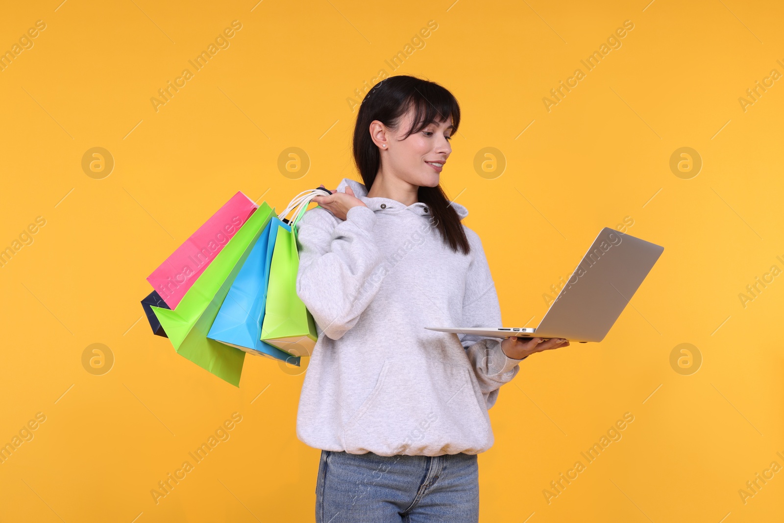 Photo of Internet shopping. Happy woman with laptop and colorful bags on orange background