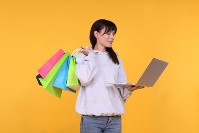 Photo of Internet shopping. Happy woman with laptop and colorful bags on orange background