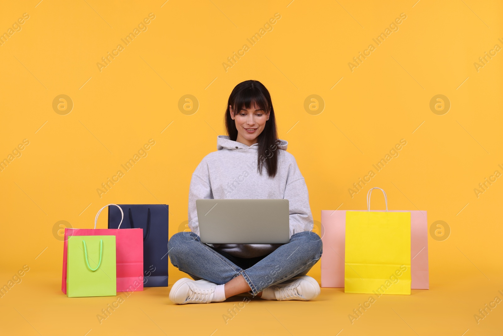 Photo of Internet shopping. Happy woman with laptop and colorful bags on orange background