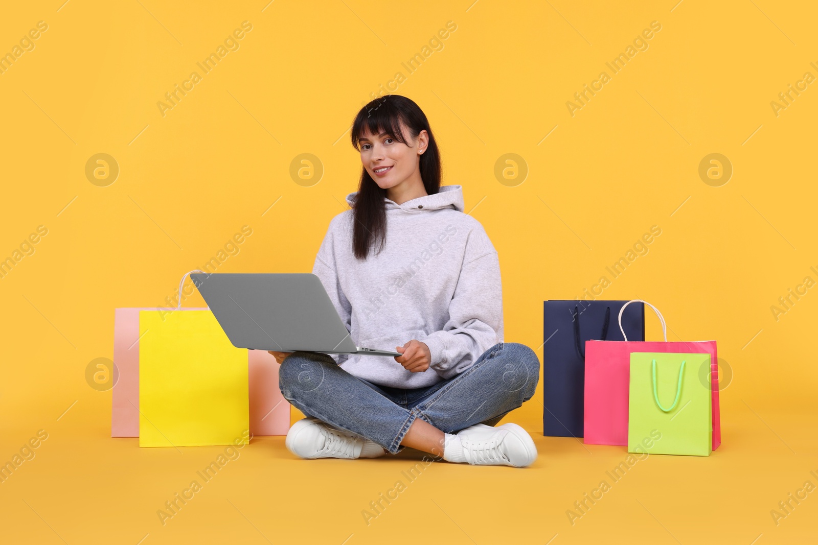 Photo of Internet shopping. Happy woman with laptop and colorful bags on orange background