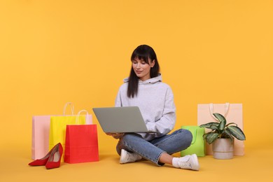 Photo of Internet shopping. Beautiful woman with laptop and colorful bags on orange background