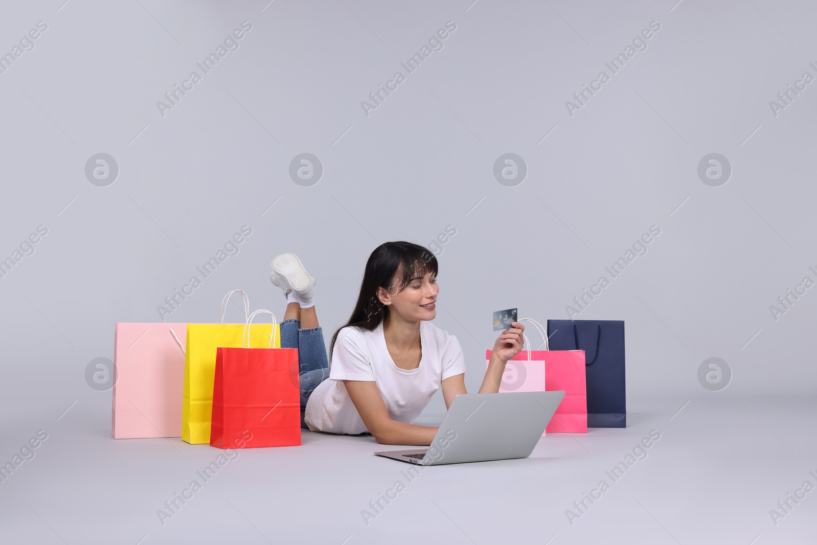 Photo of Internet shopping. Happy woman with credit card, laptop and colorful bags on grey background