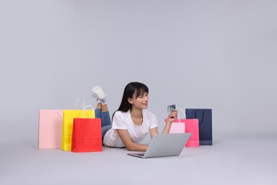 Photo of Internet shopping. Happy woman with credit card, laptop and colorful bags on grey background