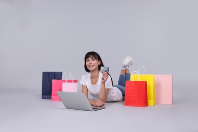 Photo of Internet shopping. Happy woman with credit card, laptop and colorful bags on grey background