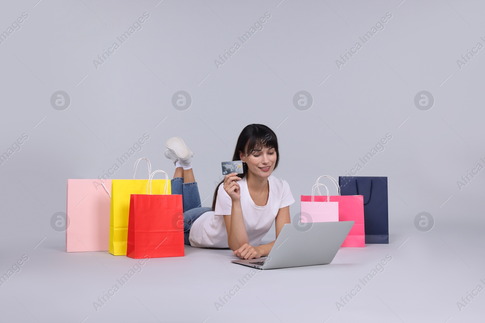 Photo of Internet shopping. Happy woman with credit card, laptop and colorful bags on grey background