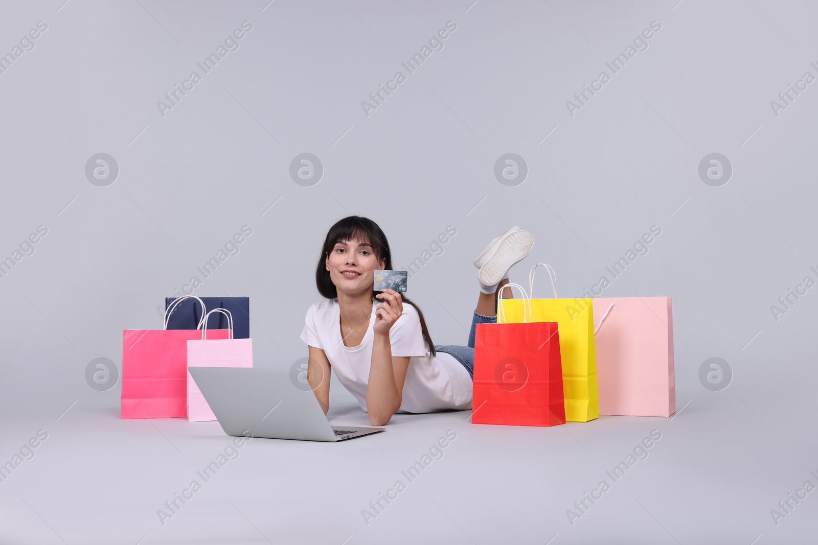 Photo of Internet shopping. Happy woman with credit card, laptop and colorful bags on grey background