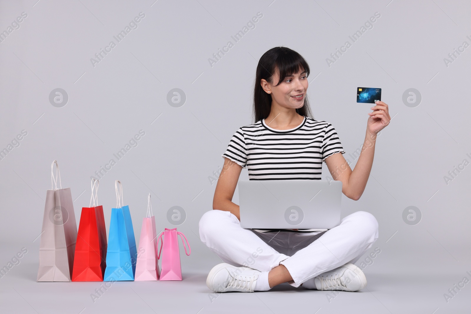 Photo of Internet shopping. Happy woman with credit card, laptop and colorful bags on grey background