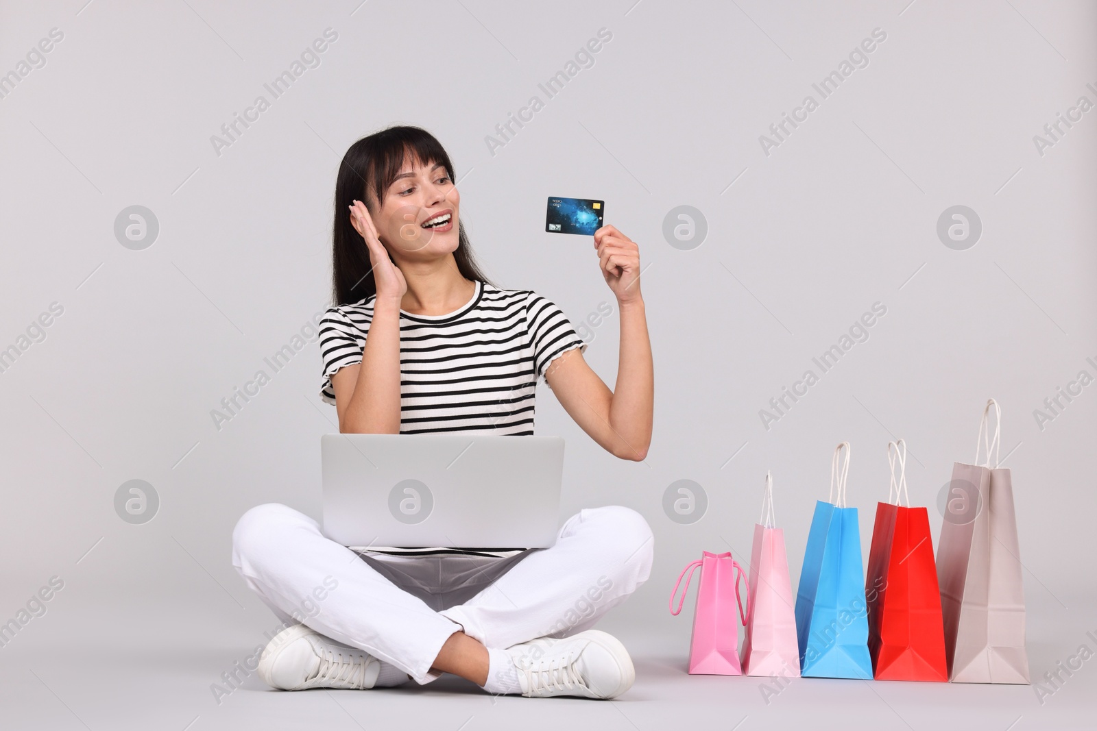 Photo of Internet shopping. Happy woman with credit card, laptop and colorful bags on grey background