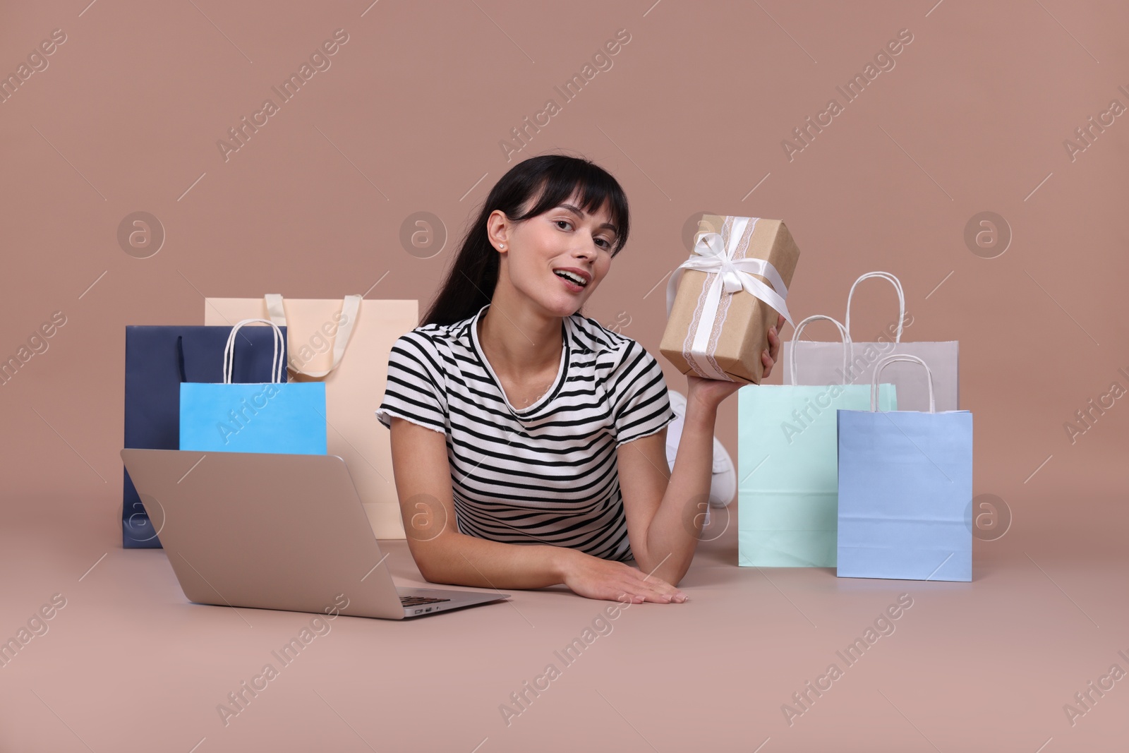 Photo of Internet shopping. Happy woman with gift box, laptop and colorful bags on beige background