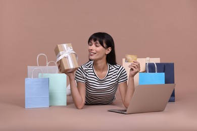 Photo of Internet shopping. Happy woman with credit card, gift box, laptop and colorful bags on beige background