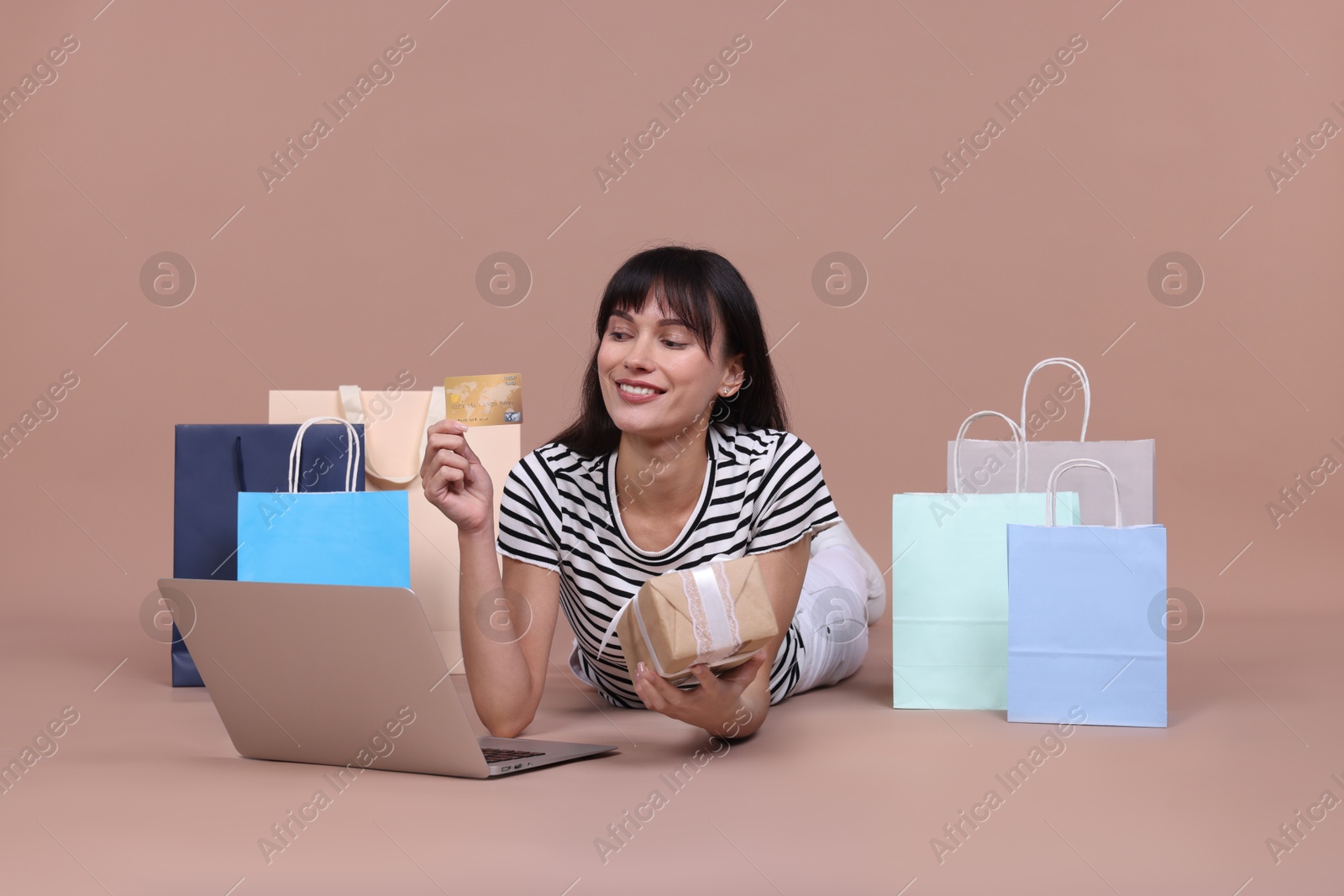 Photo of Internet shopping. Happy woman with credit card, gift box, laptop and colorful bags on beige background