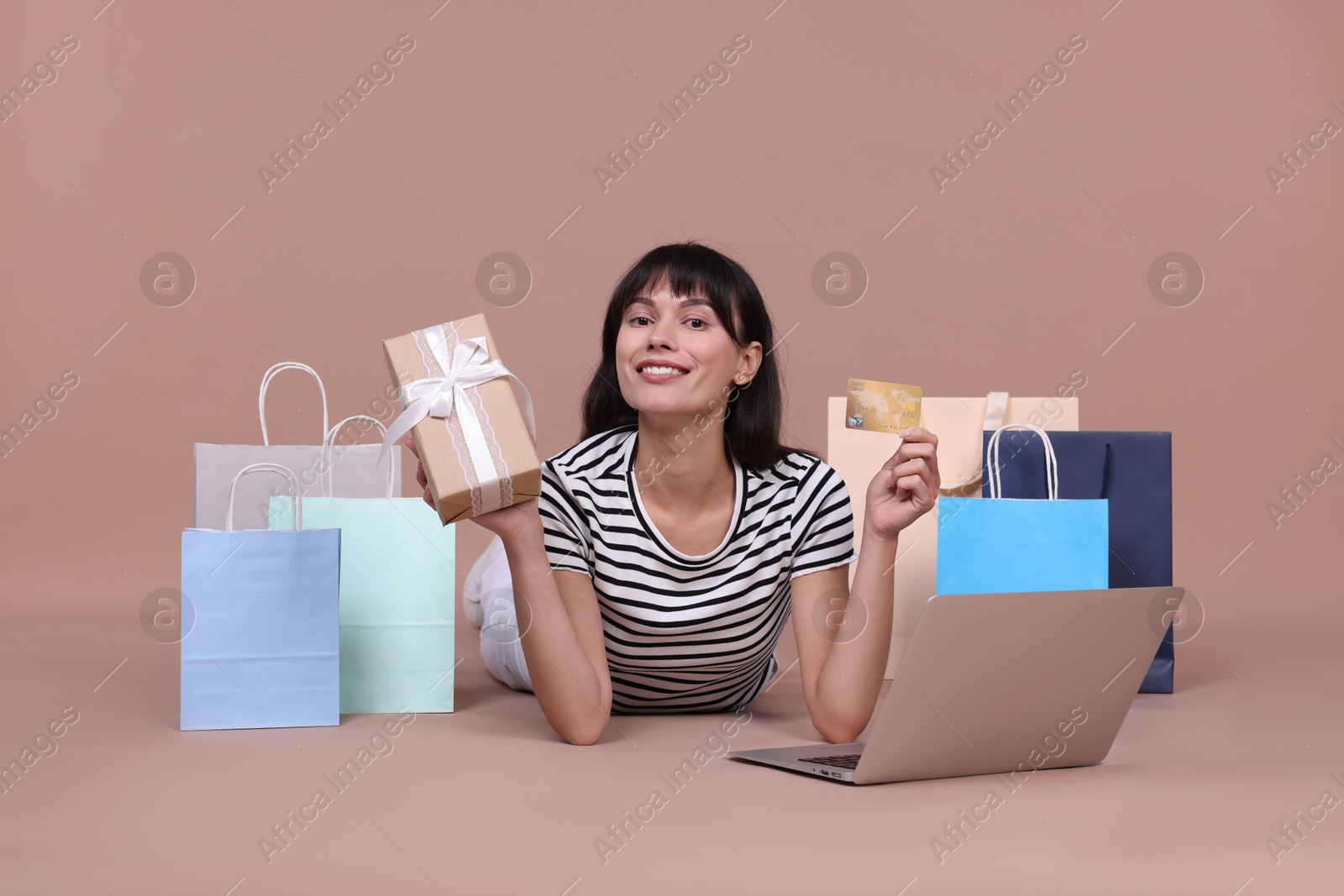 Photo of Internet shopping. Happy woman with credit card, gift box, laptop and colorful bags on beige background