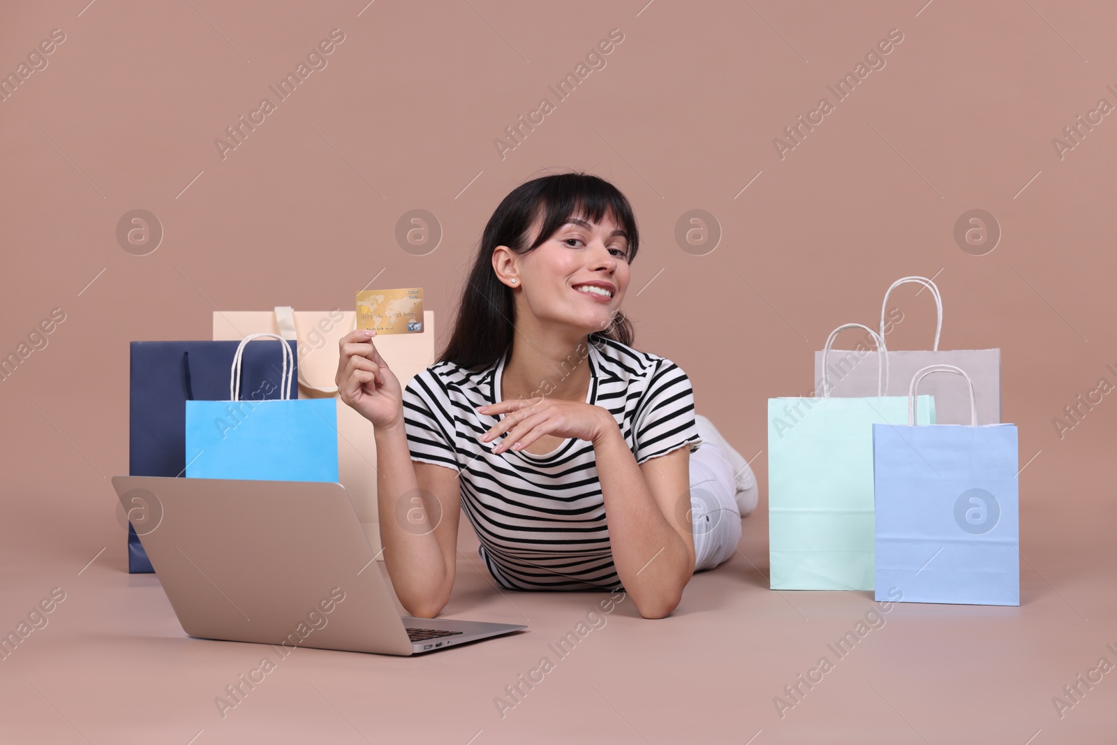 Photo of Internet shopping. Happy woman with credit card, laptop and colorful bags on beige background