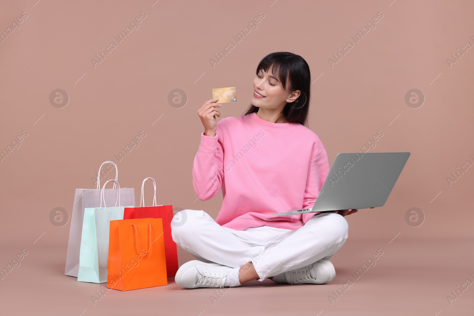 Photo of Internet shopping. Happy woman with credit card, laptop and colorful bags on beige background