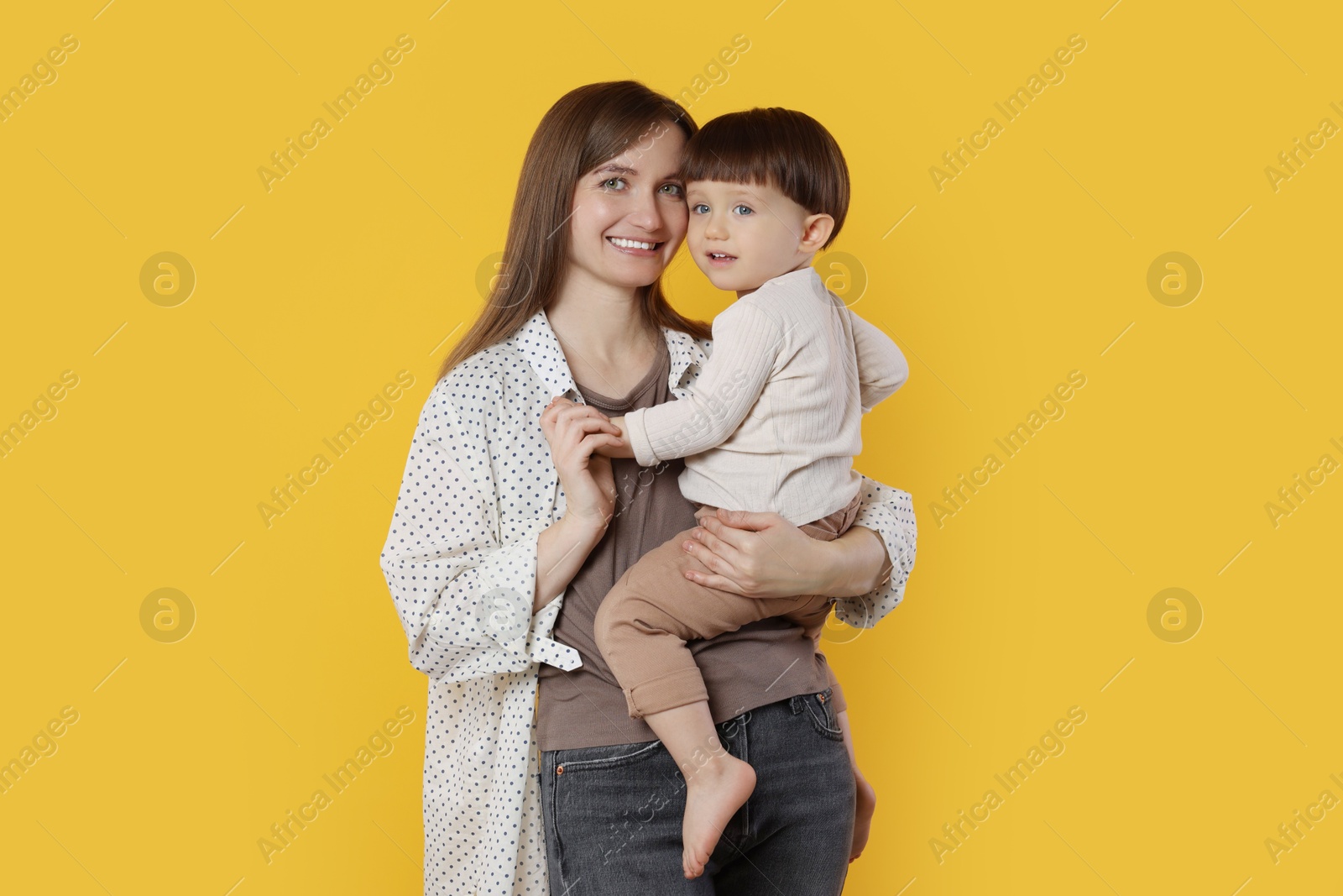 Photo of Happy mother with her cute little son on yellow background