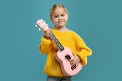 Photo of Little girl playing ukulele on light blue background