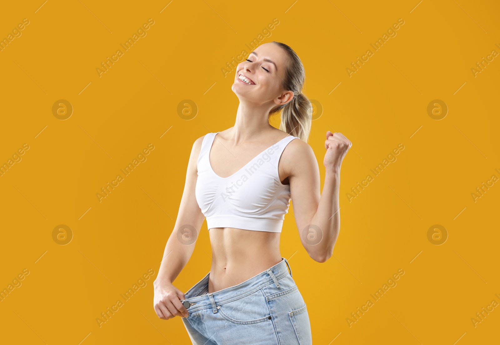 Photo of Weight loss. Happy woman wearing big jeans on yellow background