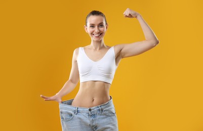 Photo of Weight loss. Happy woman wearing big jeans on yellow background