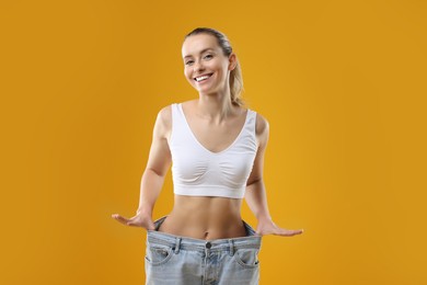 Photo of Weight loss. Happy woman wearing big jeans on yellow background