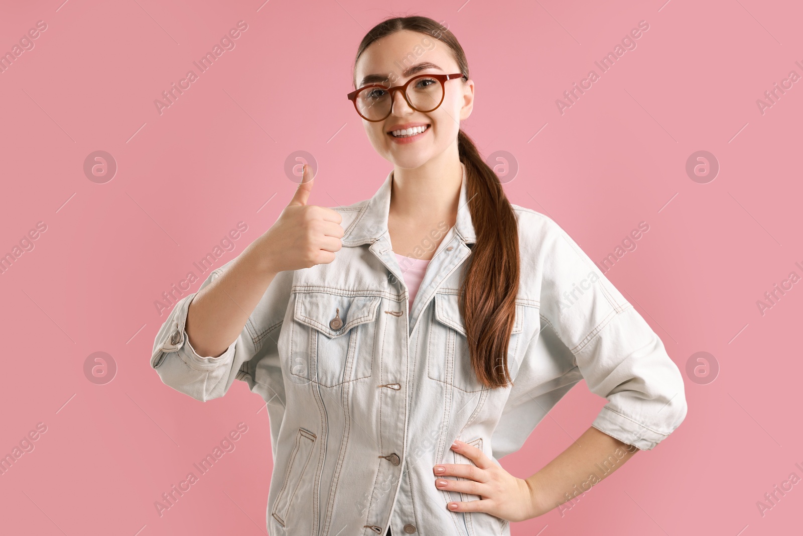 Photo of Happy woman showing thumbs up on pink background. Like gesture