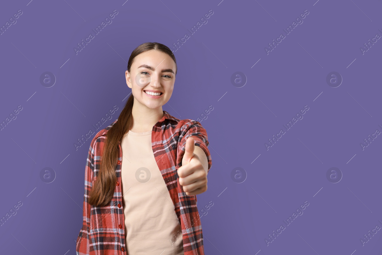 Photo of Happy woman showing thumbs up on purple background, space for text. Like gesture