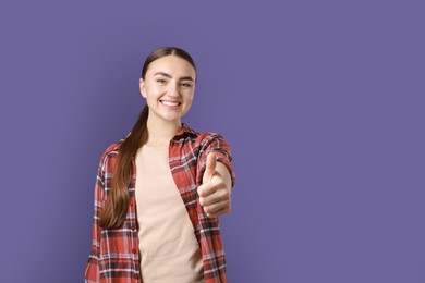 Photo of Happy woman showing thumbs up on purple background, space for text. Like gesture