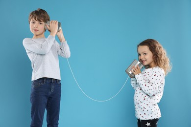 Photo of Boy and girl talking on tin can telephone against blue background