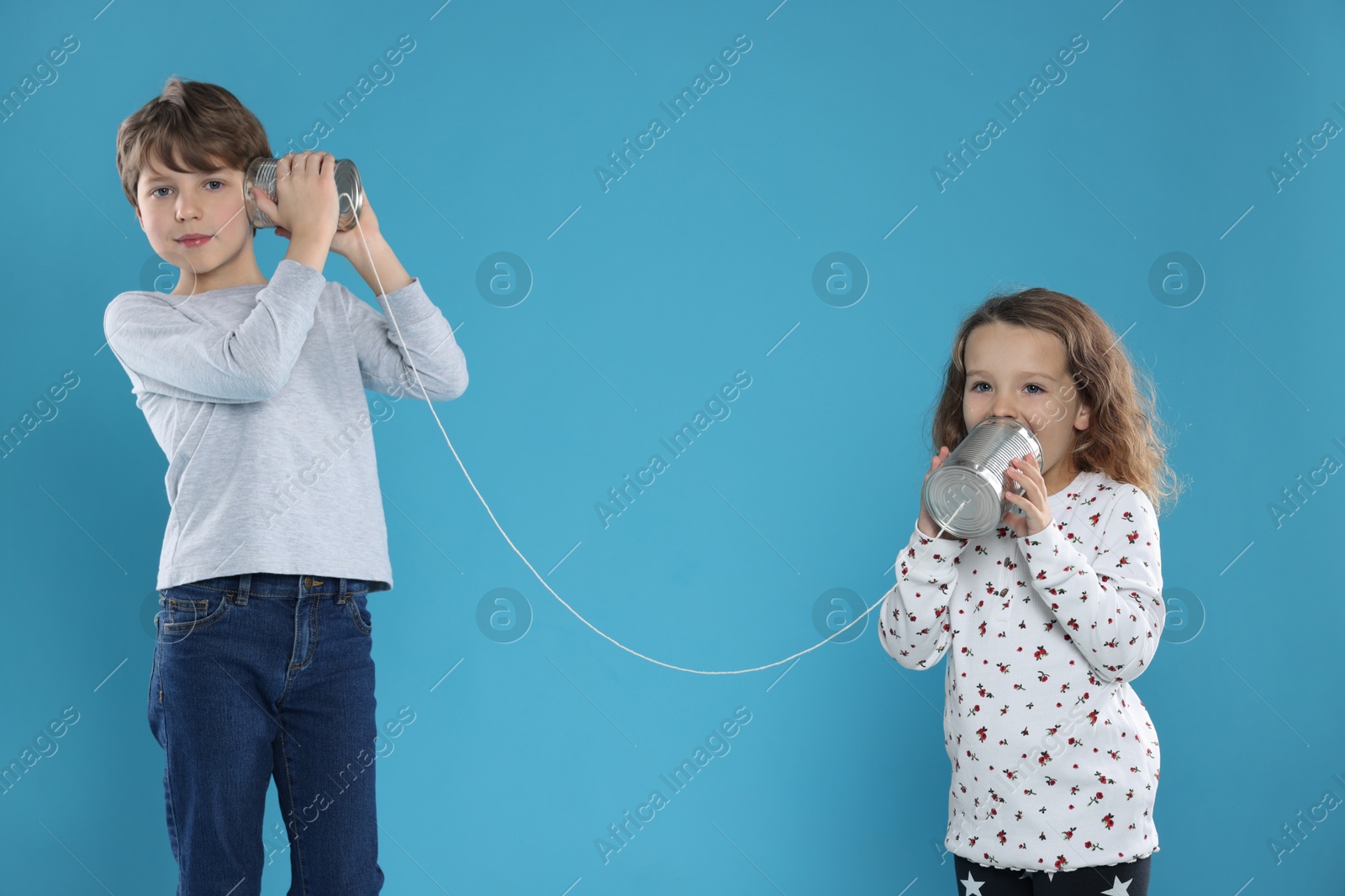 Photo of Boy and girl talking on tin can telephone against blue background