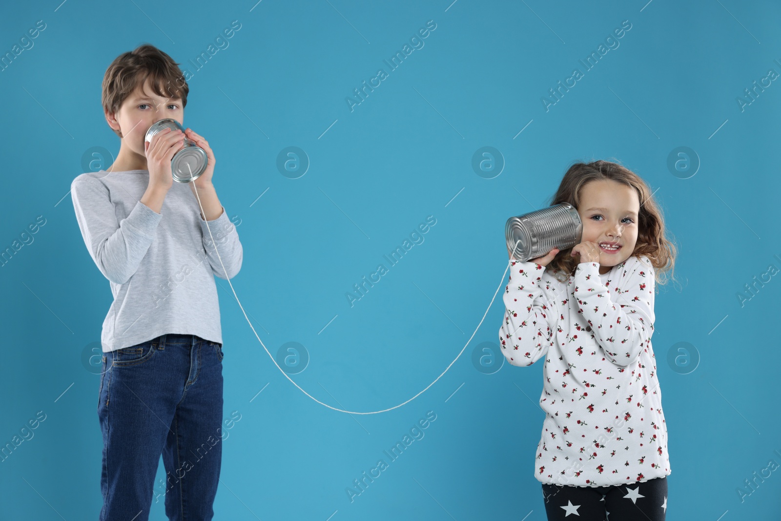 Photo of Boy and girl talking on tin can telephone against blue background