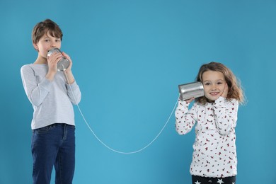 Photo of Boy and girl talking on tin can telephone against blue background