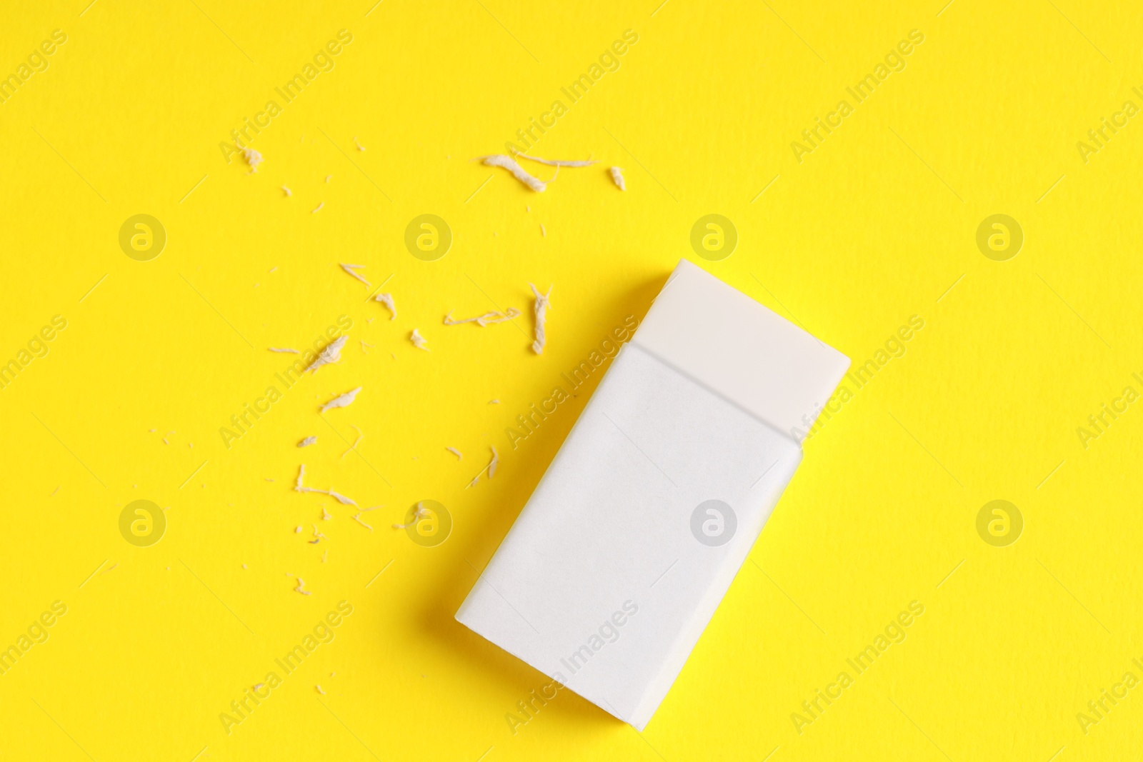 Photo of One eraser and scraps on yellow background, top view