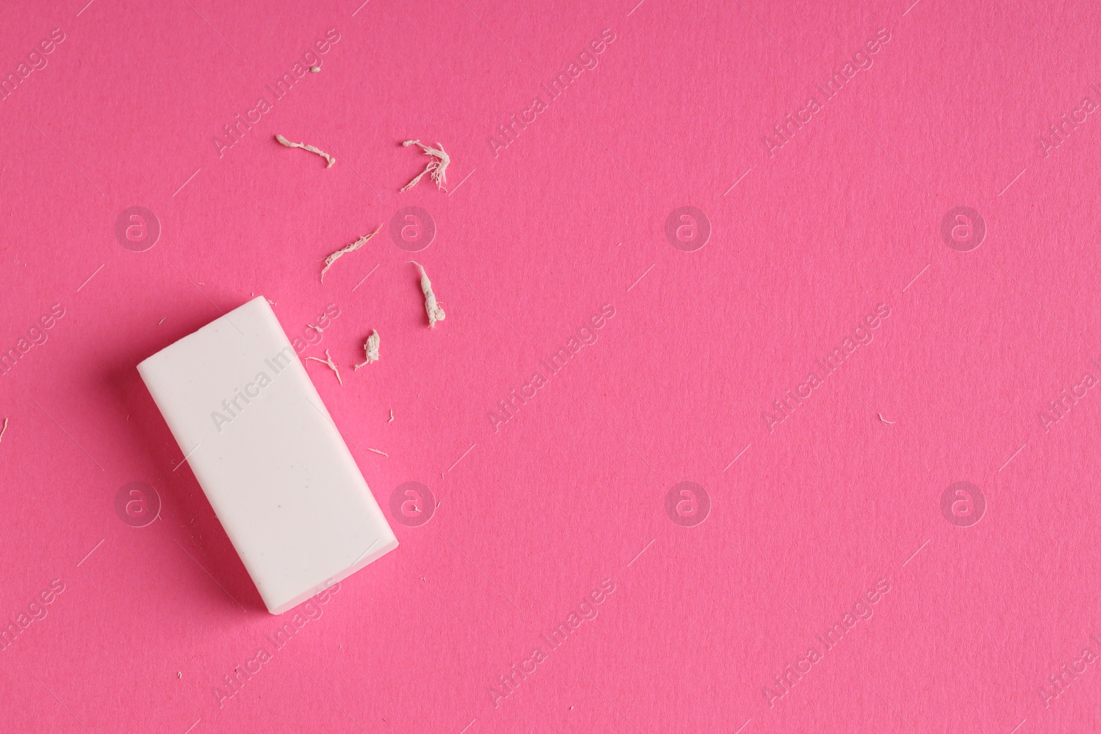 Photo of One eraser and scraps on pink background, top view. Space for text