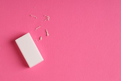 Photo of One eraser and scraps on pink background, top view. Space for text