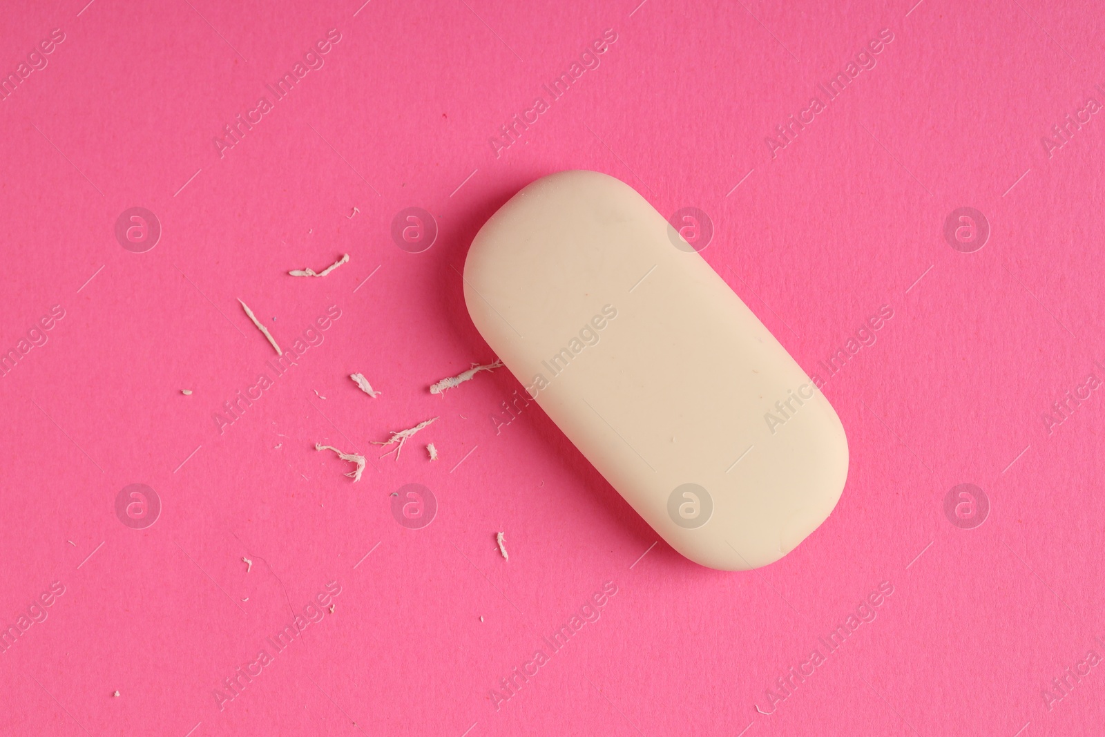 Photo of One eraser and scraps on pink background, top view