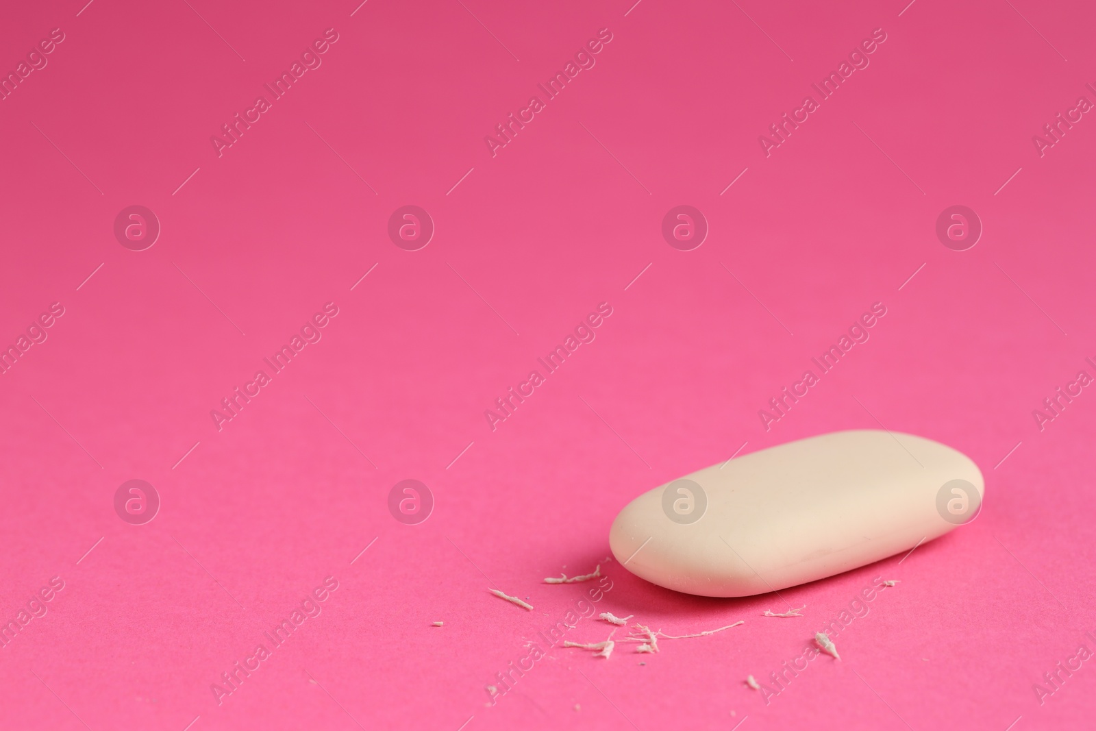 Photo of One eraser and scraps on pink background, closeup. Space for text