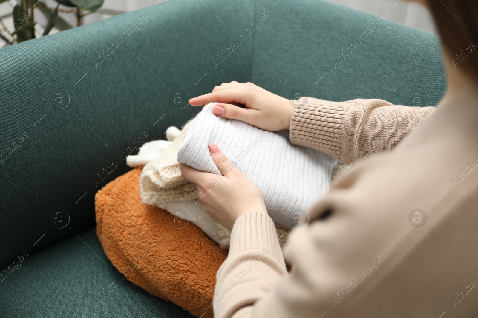 Photo of Woman stacking different used clothes on sofa indoors, closeup