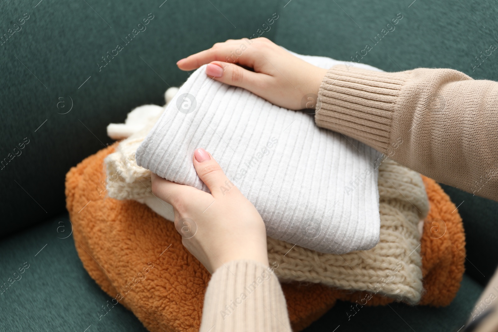 Photo of Woman stacking different used clothes on sofa indoors, closeup