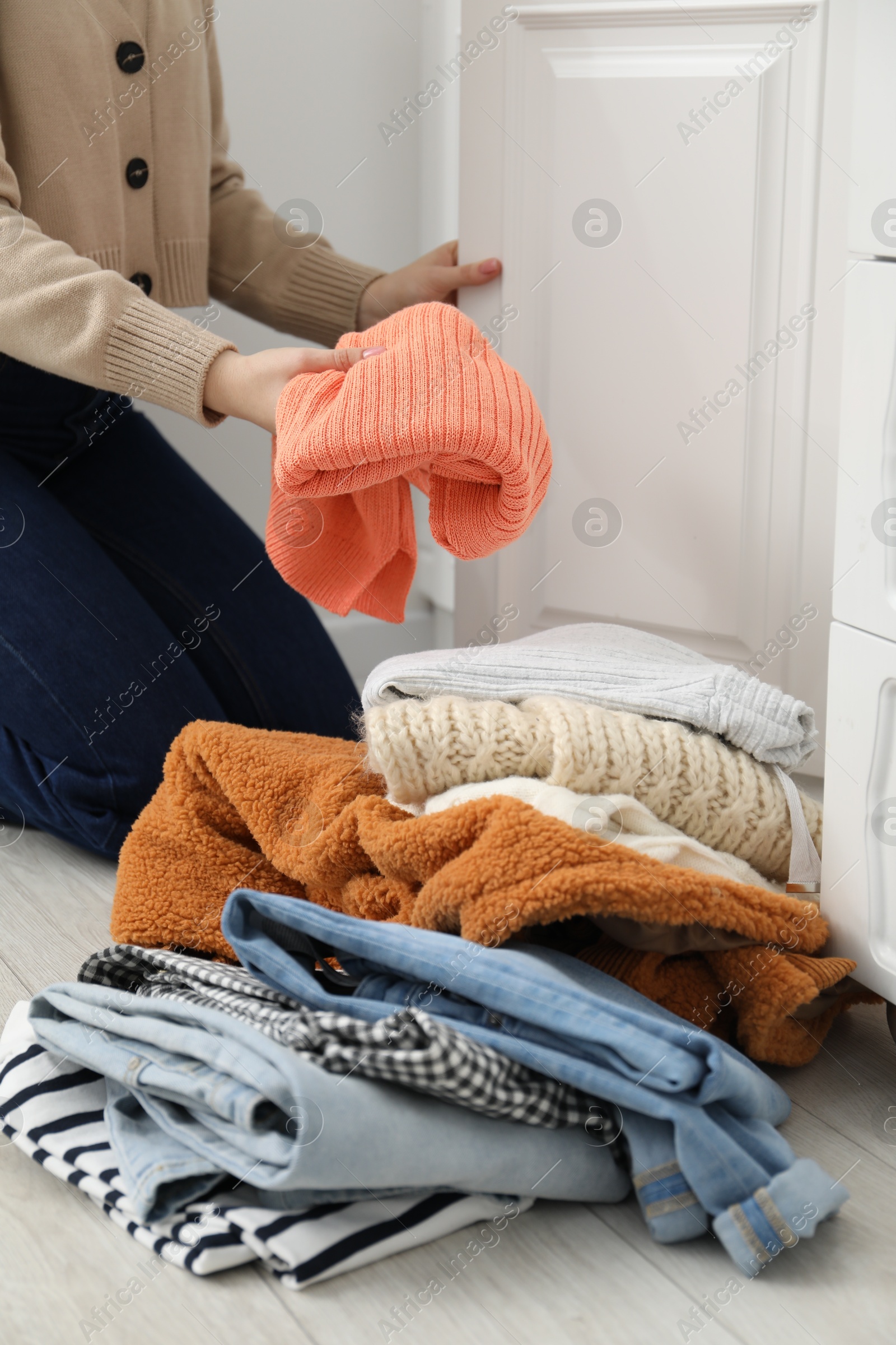 Photo of Woman with pile of different used clothes on floor indoors, closeup