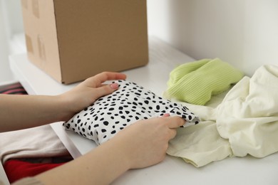 Photo of Woman stacking used clothes at chest of drawers indoors, closeup