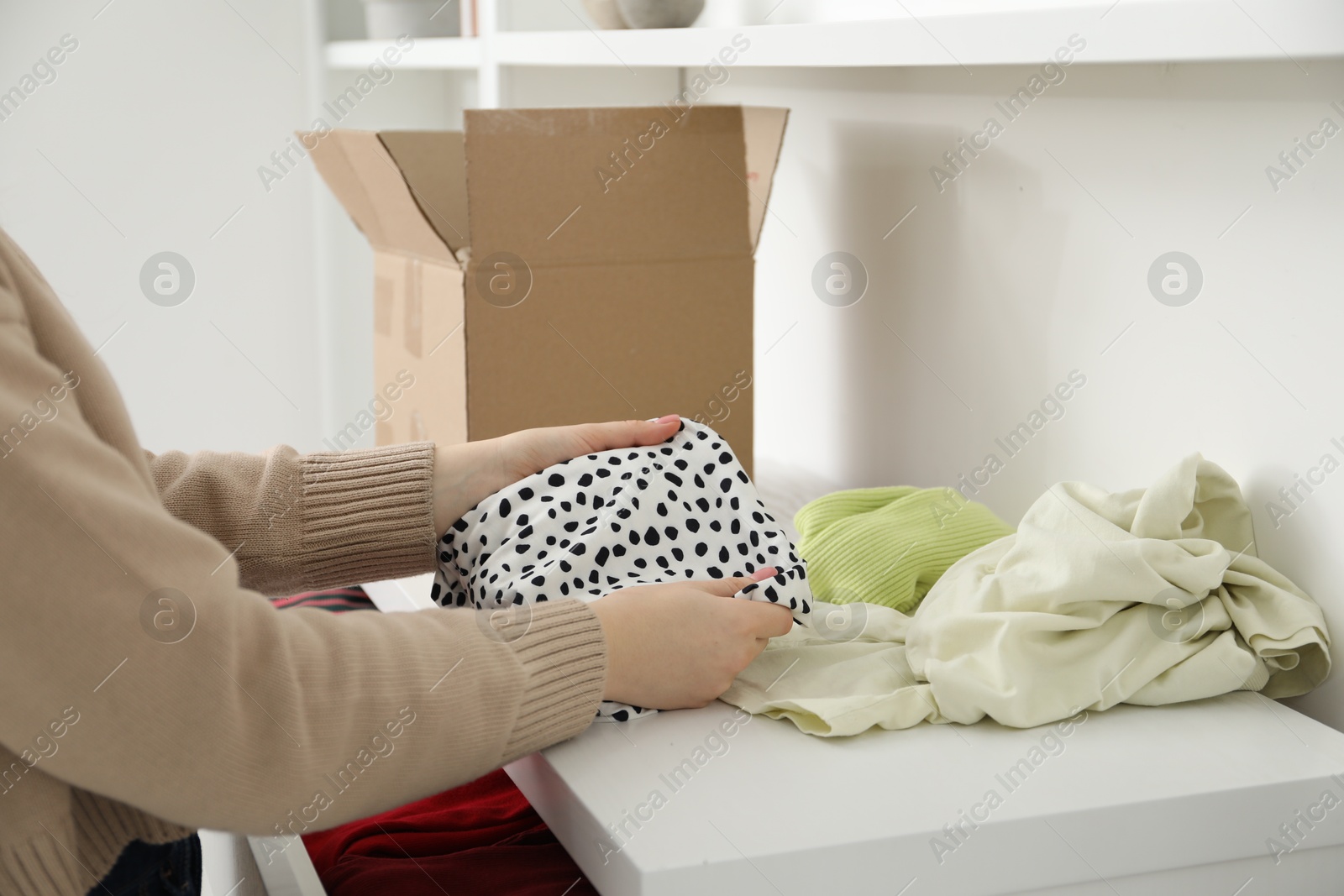 Photo of Woman stacking used clothes at chest of drawers indoors, closeup