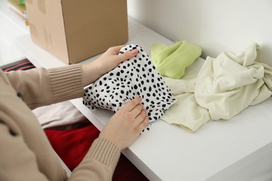 Photo of Woman stacking used clothes at chest of drawers indoors, closeup