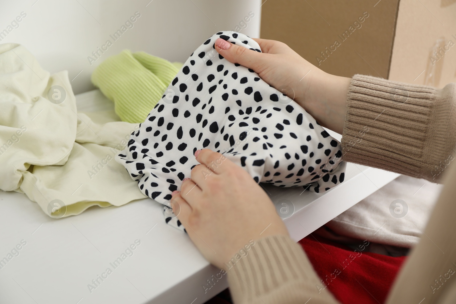 Photo of Woman stacking used clothes at chest of drawers indoors, closeup