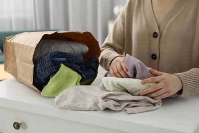 Photo of Woman organizing used clothes at chest of drawers indoors, closeup