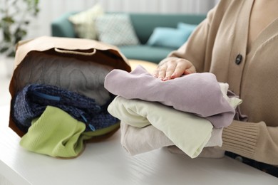 Photo of Woman organizing used clothes at white counter indoors, closeup