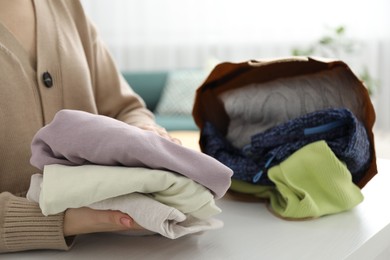 Photo of Woman organizing used clothes at white counter indoors, closeup