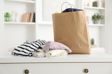 Photo of Used clothes and paper bag on chest of drawers indoors