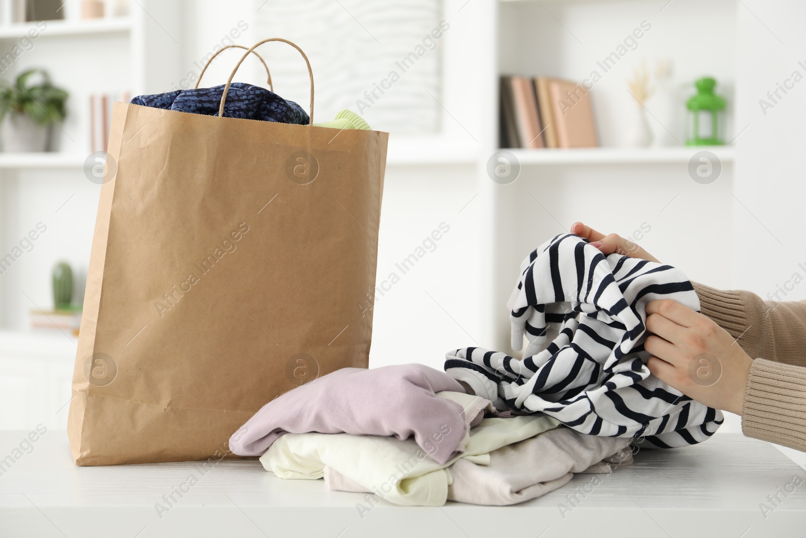 Photo of Woman organizing used clothes at white counter indoors, closeup