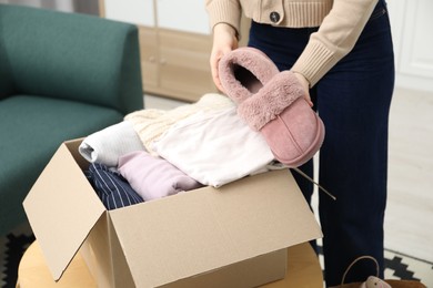 Photo of Woman putting slippers into box with used clothes indoors, closeup