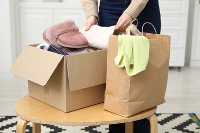 Photo of Woman stacking used clothes into box at coffee table indoors, closeup