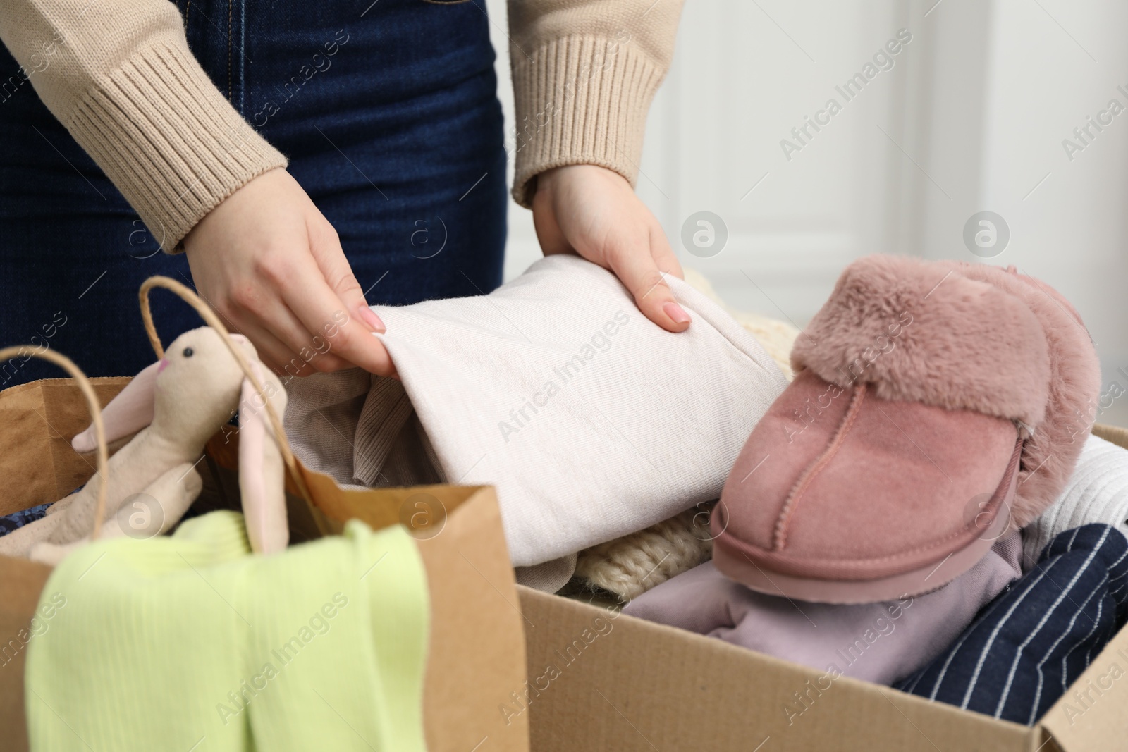 Photo of Woman stacking used clothes into box indoors, closeup